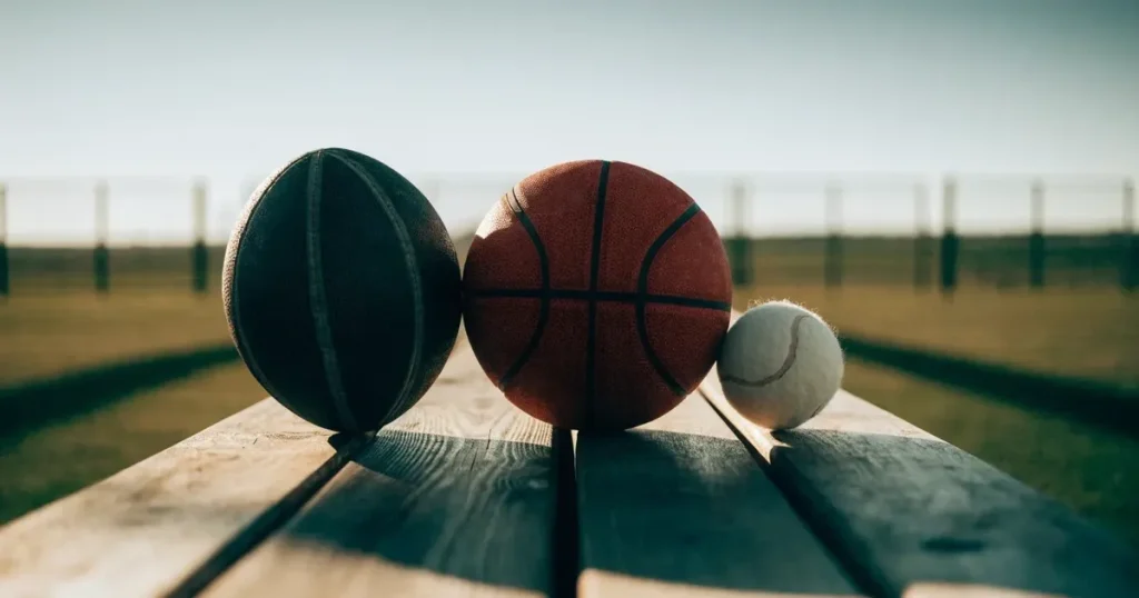 Tre palloni di sport diversi allineati uno accanto all'altro su una panca di legno