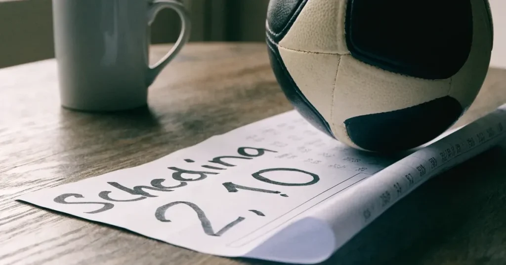 Un pallone da calcio appoggiato su una schedina bianca su un tavolo di legno, alla luce del giorno